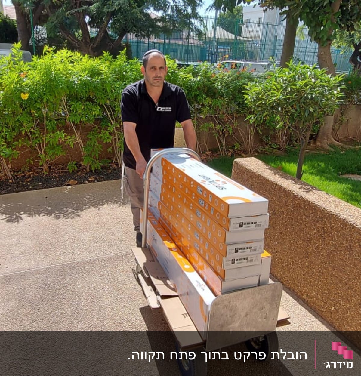 אדם דוחף עגלת משא עם קופסאות על שביל